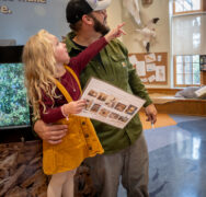 Father with young daughter pointing excitedly at bird exhibit.