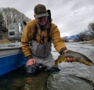 Man outside a fishing boat holding a trout